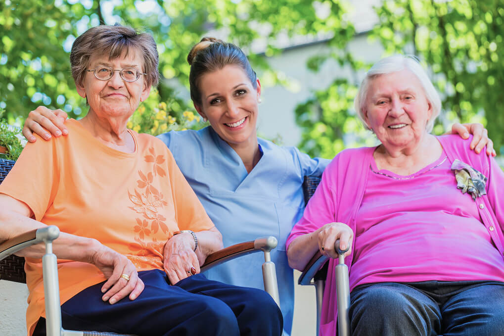 Pflegerin mit zwei Seniorinnen im Garten